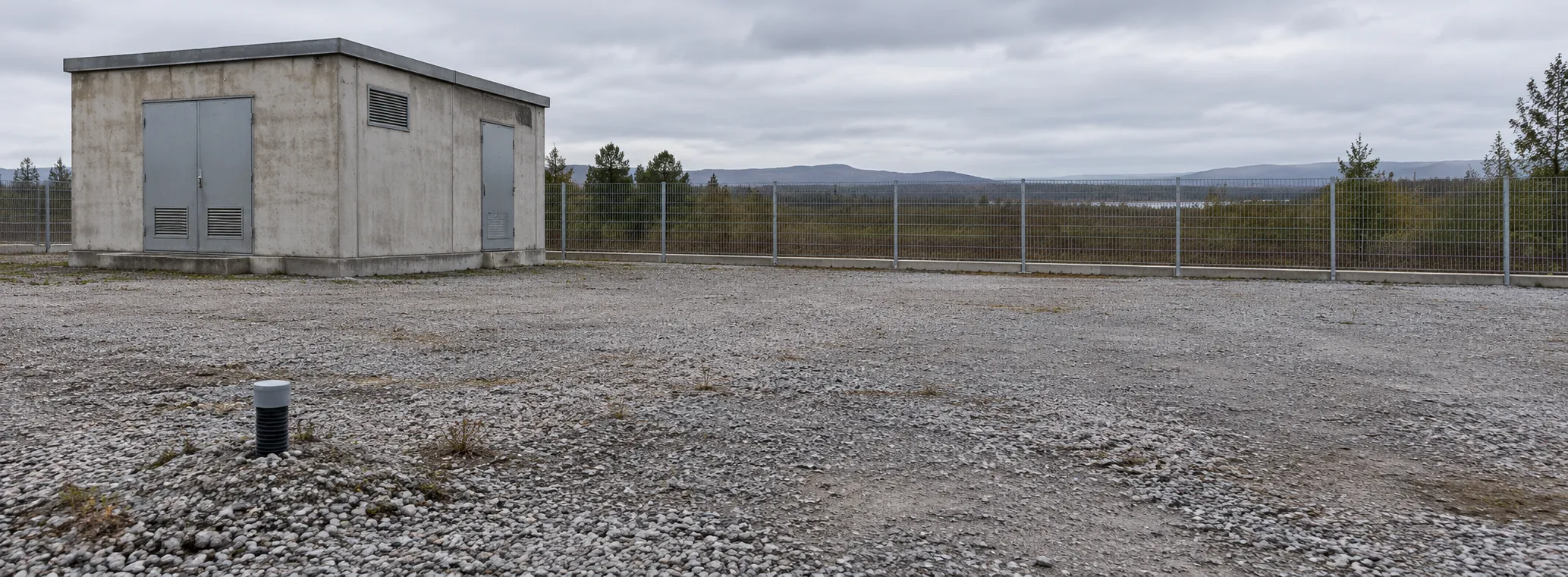 Unused gravel plot beside a small transformer building with a fence and a capped cable conduit