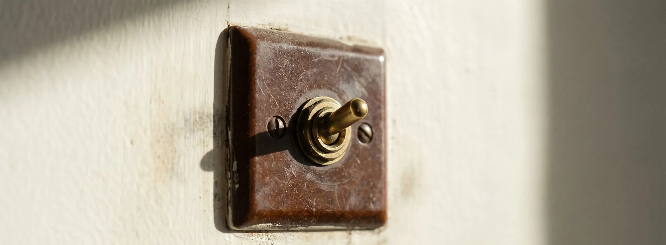 Alter Kippschalter aus Messing auf einer weiß gestrichenen Wand