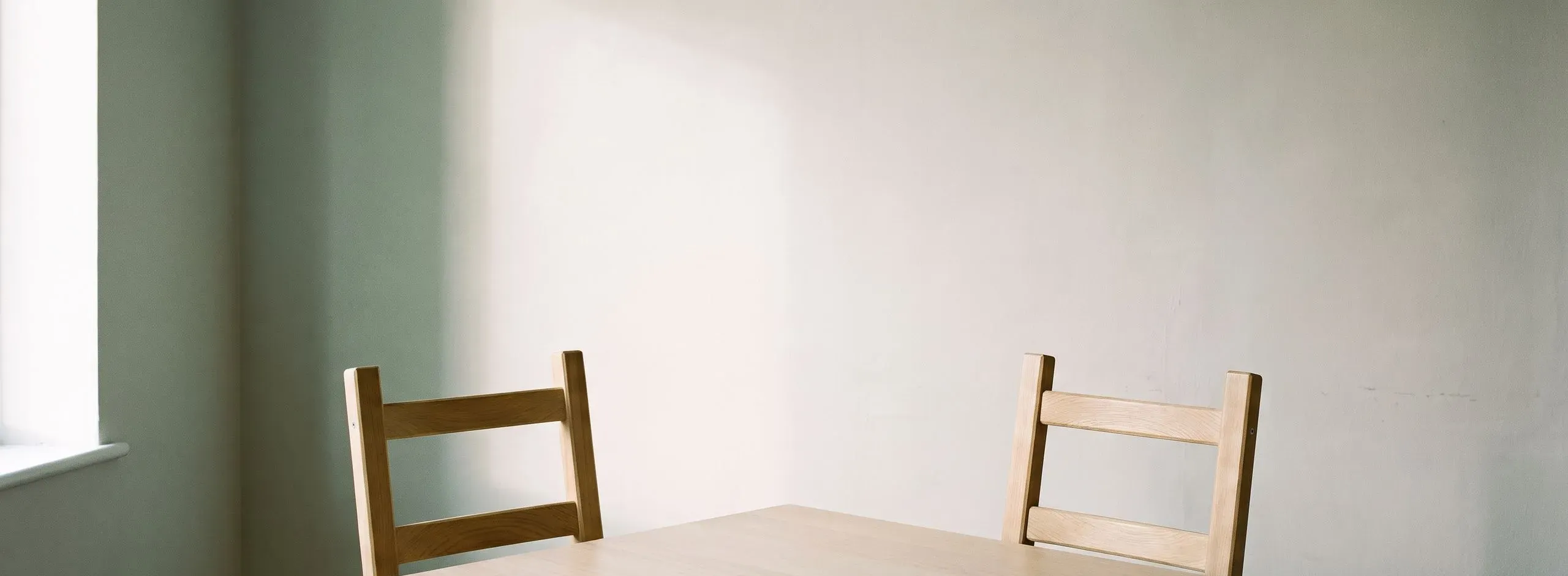 Zwei Stuhllehnen an einem hellen Holztisch vor einer schlichten Wand