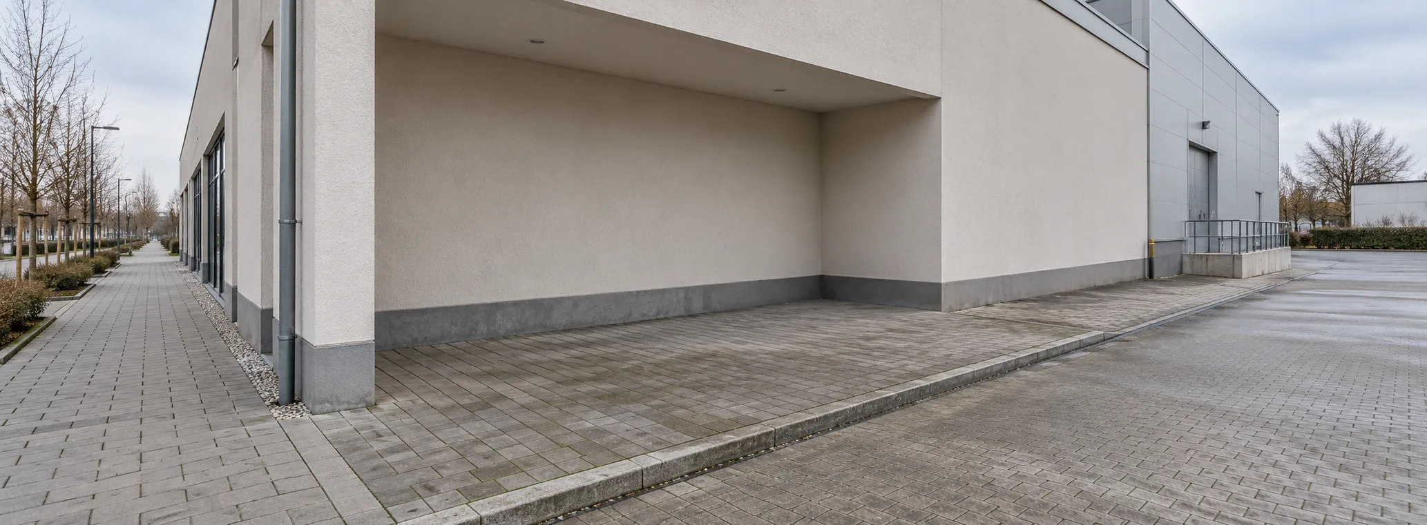 Empty paved recess beside a commercial building with a footpath and a delivery approach to the side