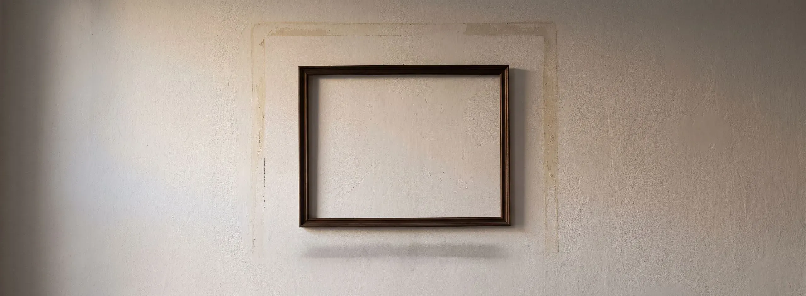 Leerer Bilderrahmen an einer Putzwand, umgeben vom Abdruck eines größeren Bildes
