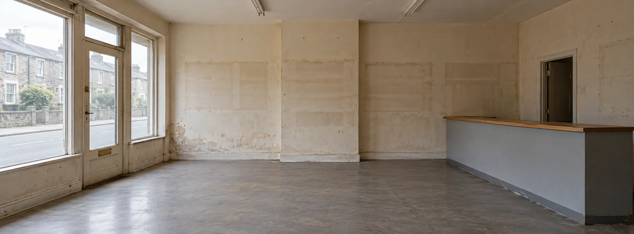 Vacant shop with a broad storefront window, an old counter and marks from former shelving on the wall