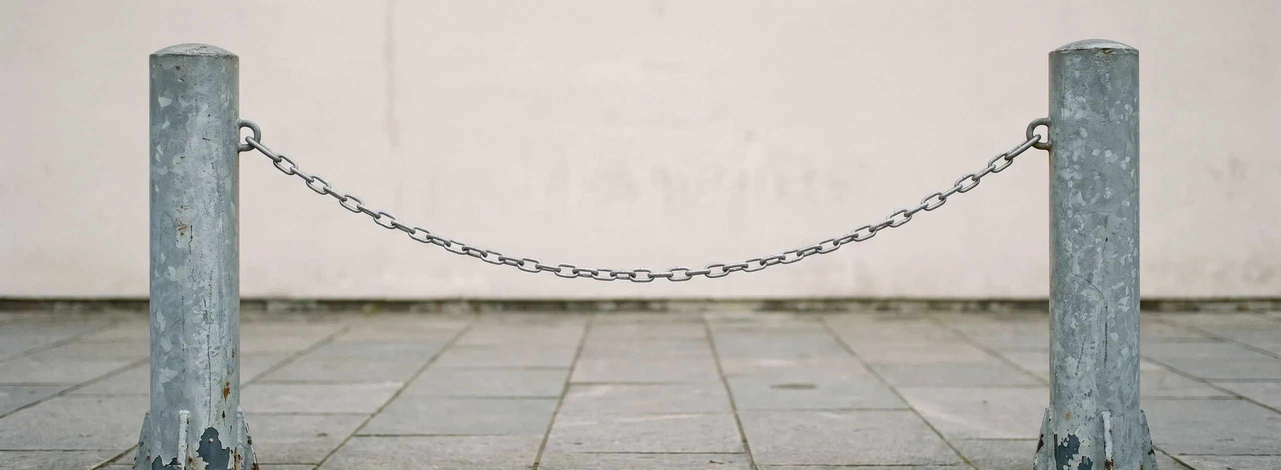 Zwei Absperrpfosten mit durchhängender Kette auf einem gepflasterten Vorplatz